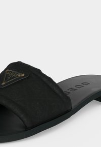 Μαύρα σανδάλια slide με φαρδιά υφασμάτινη λωρίδα που διαθέτει τριγωνική πλακέτα με το λογότυπο Guess και ανάγλυφη ανατομική σόλα με το όνομα της μάρκας.