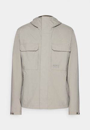 Hellgraue Jacke mit Kapuze, zwei vorderen aufgesetzten Taschen und einem Reißverschluss vorne. Glatte Textur mit minimalistischem Design und Logo-Akzent.