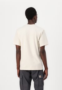 Beige bomulds t-shirt med korte ærmer, rund halsudskæring og en afslappet pasform, vist fra ryggen mod en ensfarvet hvid baggrund.