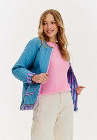 Pikowana niebieska kurtka z różowymi akcentami i w paski podszewką, zestawiona z różowym swetrem. Kurtka ma zamek błyskawiczny i kolorowe mankiety.