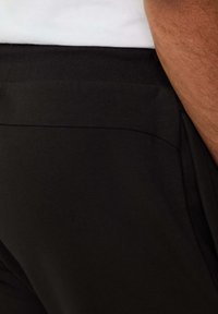 Crne pamučne jogger hlače s glatkom teksturom, koje imaju široki elastični pojas i suptilan šav uz bok.
