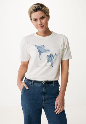 T-shirt en coton blanc avec imprimé graphique floral bleu sur le devant, col rond et manches courtes, associé à un jean taille haute bleu.