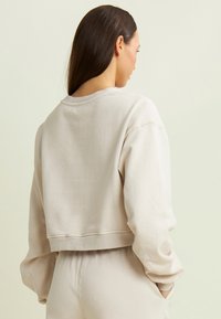 Felpa cropped beige chiaro realizzata in materiale morbido, con colletto rotondo, maniche lunghe e polsini a costine.