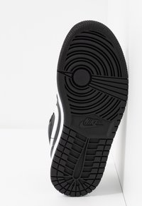 Semelle extérieure en caoutchouc noir d'une chaussure Nike montrant des motifs de bandes de roulement circulaires et en grille avec le logo Nike près du milieu de la semelle.