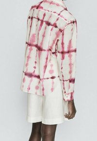Lightweight, long-sleeve shirt with pink and maroon tie-dye patterns on a cream background; paired with white linen shorts.
