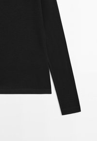 Chemise noire à manches longues avec un ourlet droit et une petite fente latérale du côté droit, présentée sur un fond blanc.