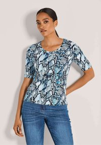 Kurze Ärmel Bluse mit einem blau-schwarz Schlangenmuster, runder Halsauschnitt und figurigem Design. Kombiniert mit blauen Jeans.