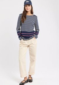 Camicia a righe navy e crema a maniche lunghe con scollo a barca e dettagli con bottoni, abbinata a pantaloni beige e scarpe flat nere.