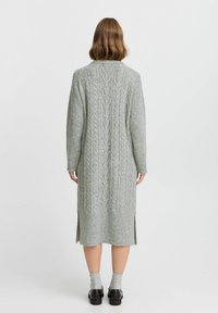 Larga chaqueta de punto gris con diseño de trenzas, aberturas laterales, textura acanalada y corte recto.