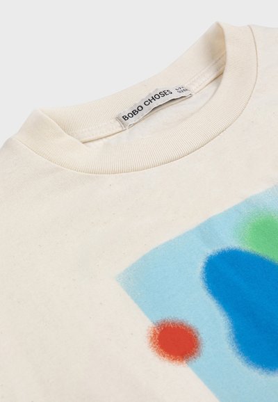 Cream-colored T-shirt with a ribbed crew neck and abstract print in blue, green, and red near the bottom right.