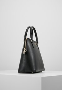 Černá kožená kabelka s texturovan ým povrchem, zaoblenými uchy, zlatými zipy a trojúhelníkovým tvarem, vystavená na bílé podstavě.