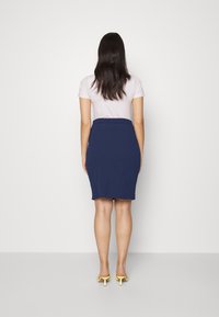 Námorně modrá pletená tužková sukně s texturovanou látkou, elastickým pasem, spárovaná se světle růžovým tričkem a žlutými pantofli. Pohled zezadu.