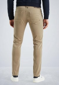 Pantalones de algodón beige con un corte ajustado, que cuentan con bolsillos traseros y un sutil logotipo en la cintura. Llevados con zapatillas blancas.
