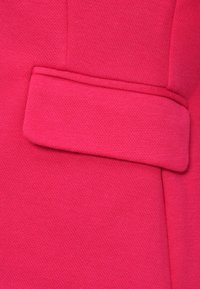 Gros plan d’un tissu rose texturé avec un détail de rabat rectangulaire cousu sur la surface.