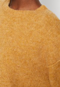 Gul ulltröja med en mjuk, texturerad finish och rund halsringning, med synliga stickade mönster och en avslappnad passform.