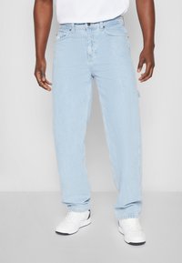 Light blue denim jeans with a relaxed fit, five-pocket design, and a button fly. Worn with white sneakers, showcasing a clean finish.