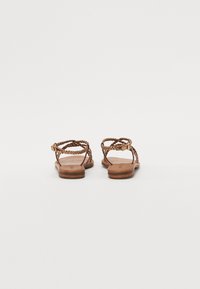 Sandales en cuir tressé marron avec une semelle plate, dotées de bretelles tissées et d'une fermeture à boucle pour un ajustement sécurisé. Design simple et fonctionnel.