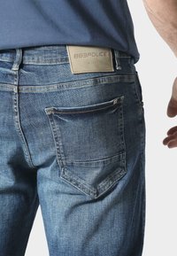 Jeans de mezclilla en un lavado medio con una textura suave, que cuentan con bolsillos traseros y una etiqueta de cuero con la marca en la cintura.