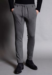 Grå sweatpants med dragsko i midjan, fickor och en snäv passform, tillsammans med svarta ankelstövlar. Slät textur.