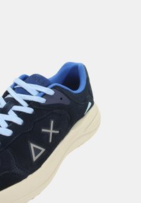 Sneaker blu navy con dettagli in suede e mesh, lacci azzurri chiari e suola bianca a contrasto. Presenta accenti geometrici sui lati.