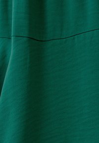 Green textured fabric with a smooth surface. Features a horizontal seam across the midsection. Soft drape with subtle sheen.