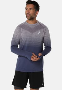 Långärmad atletisk topp i gradientgrått till marinblått, med meshtextur på axlarna, tumhål och logotypdetalj på bröstet.