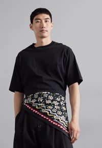 Black oversized t-shirt with short sleeves, paired with a patterned waist belt featuring daisies, wavy lines, and a red accent.