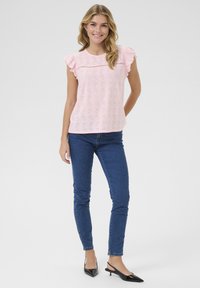 Lys pink, kortærmet top med bølgede kanter, der har øjenlågskontrol detaljer. Parret med blå stramme jeans og sorte slingback hæle.