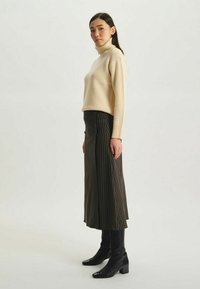 Pull à col roulé beige à côtes associé à une longue jupe à rayures sombres. La mannequin porte des bottes noires à talons hauteur genou. Design minimaliste.