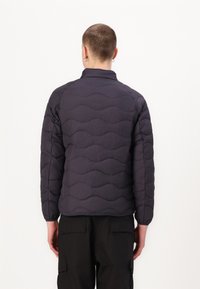 Veste matelassée bleu marine foncé avec un motif de vagues, un col haut et des manches longues, fabriquée dans un tissu léger et texturé.