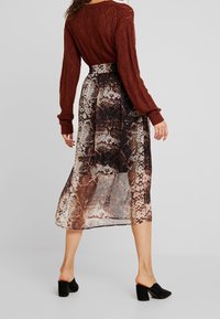 Red knitted sweater with long sleeves paired with a pleated, mid-length skirt featuring a brown and beige snake print design. Black heeled mules.