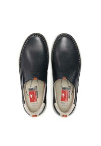 Zapatos negros de cuero tipo mocasín con paneles elásticos en los laterales, suela blanca, costuras en contraste y un acento naranja cerca del talón. Etiquetas visibles en el interior.