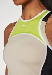 Canotta sportiva con un design aderente caratterizzata da pannelli di un beige chiaro, nero e verde vibrante. Include un dettaglio del logo bianco nella parte anteriore.