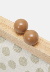 Two brown spherical beads on a light wooden clasp with beige polka-dot fabric attached, set against a white background.