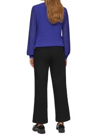 Paarse trui met geribbelde mouwen, gecombineerd met zwarte wijde broek en zwarte schoenen. De outfit is van achteren bekeken.