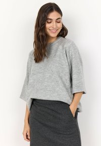 Jasnoszary, oversize sweter pleciony z okrągłym dekoltem i obniżonymi szwami ramion. Noszony z ciemną, teksturowaną spódnicą ołówkową.