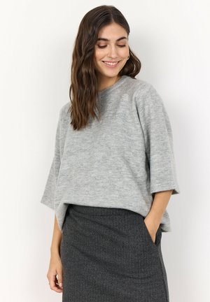 Jasnoszary, oversize sweter pleciony z okrągłym dekoltem i obniżonymi szwami ramion. Noszony z ciemną, teksturowaną spódnicą ołówkową.