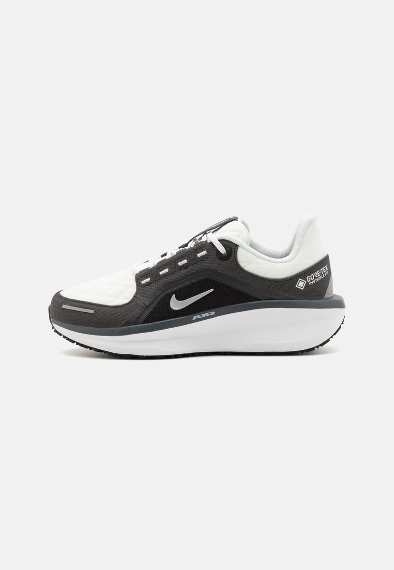 Zapatilla deportiva en blanco y negro con un upper texturizado, cuello acolchado, cierre de cordones y una prominente unidad de aire gris en la suela.
