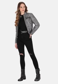 Grå faux læderjakke med en lynlåslomme, høj krave og struktureret overflade, parret med sorte ripped jeans og ankelstøvler.