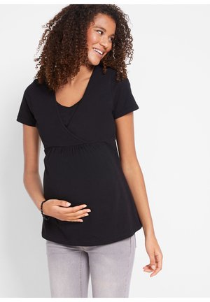 Top materno nero con maniche corte, design incrociato davanti, scollatura a V e vita arricciata, abbinato a pantaloni grigio chiaro.