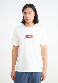Balta medvilninė t-shirt su ryškiu grafiniu dizainu centre. Trumpi rankovės ir apvalus kaklo iškirpimas. Suderinta su mėlynomis kelnėmis.