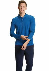 Langärmliges blaues Polohemd mit Kragen, Drei-Knopf-Leiste und lässigem Schnitt, kombiniert mit dunkelblauen Hosen.