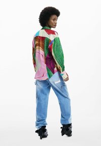 Kleurrijk overhemd met patroon in tinten van roze, groen en bruin; gecombineerd met lichtblauwe spijkerbroek en zwarte laarzen met hak.