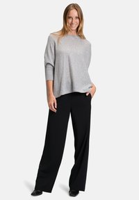 Svetle šedý oversized svetr s třičtvrtečními rukávy, spárovaný s černými kalhotami s širokými nohavicemi. Hladká textura, ležérní design, uvolněný střih.