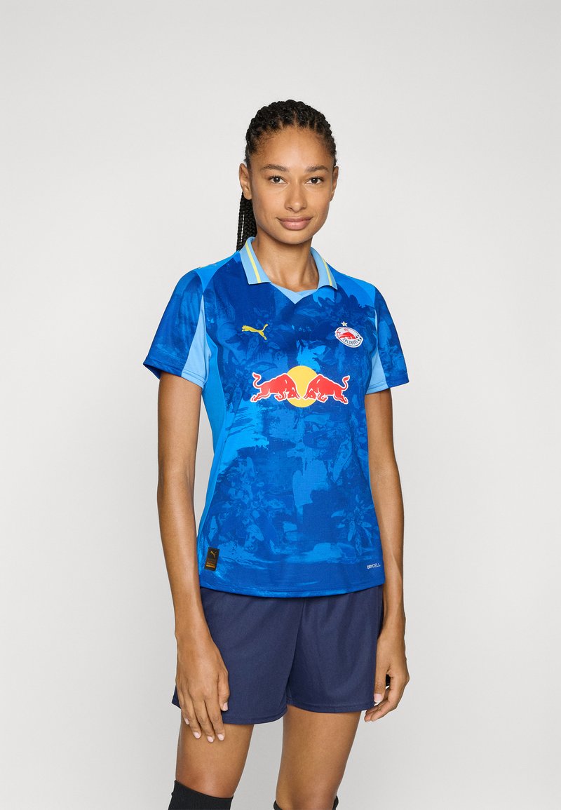 Maglia da calcio blu con maniche corte, colletto e logo Red Bull sul davanti. Presenta un design a gradiente e accenti di blu chiaro a contrasto.