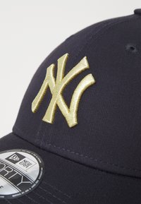 Navy cap featuring a stitched gold New York Yankees logo. Fabric is structured, with a curved visor and an adjustable strap at the back.