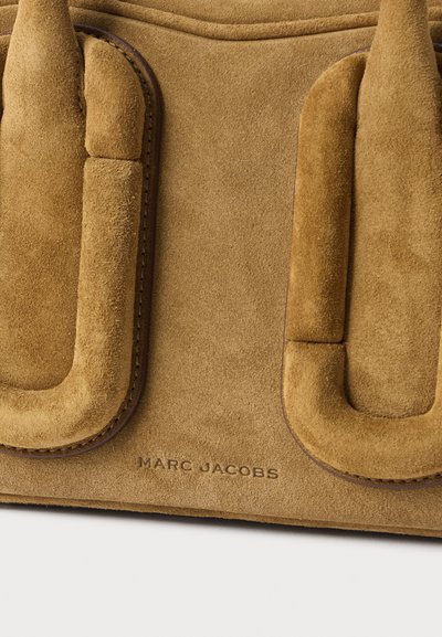 Sac à main en daim marron avec des poignées rembourrées arrondies et le logo Marc Jacobs embossé près du centre inférieur.