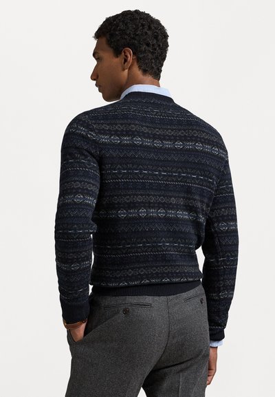 Navy patterned sweater with a crew neck, textured fabric, ribbed cuffs, and hem. Paired with gray tailored trousers featuring back pockets.