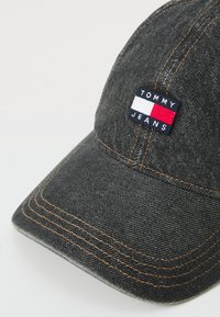 Boné de basebol em denim escuro com faixa costurada, fio laranja contrastante e um logótipo bordado retangular da Tommy Jeans em azul, branco e vermelho.