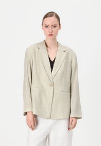 Beige lina bleiser, mille madal krae, ühe nupuga kinnitamine ja eesmine taskud. Selles on peened vertikaalsed triibud ja pikad küllused.